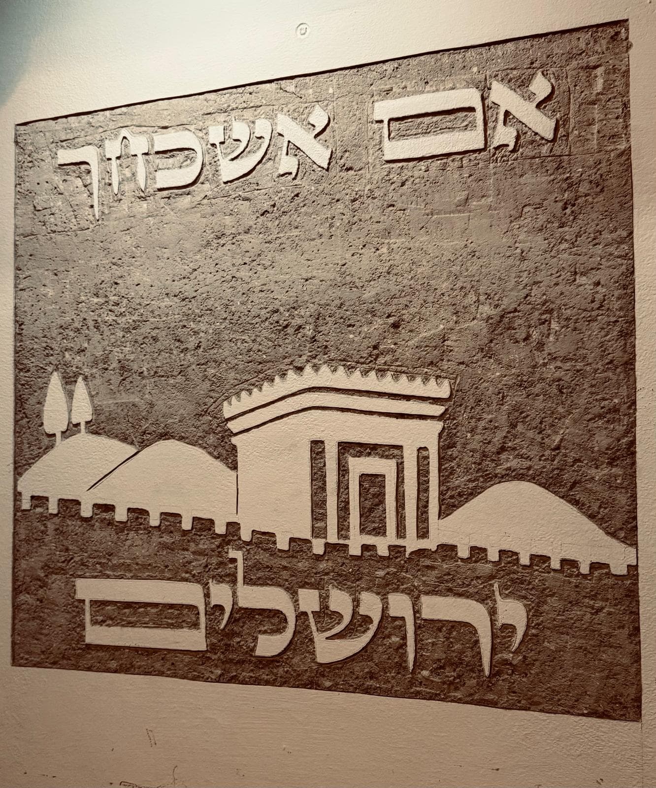 סיתות קיר בגוון בז' חם: הכיתוב 'אם אשכחך' מסותת בחלקו העליון, ובמרכז נראה בית המקדש מוקף בהרי ירושלים ובעצי אורן, עם שבילי קווים זורמים בקדמת התמונה.